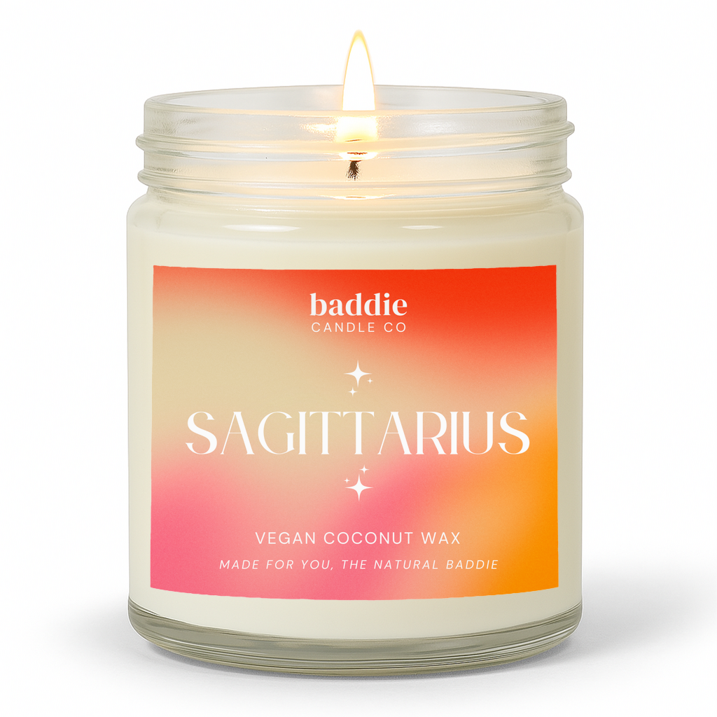 A clear jar candle with a colorful pink hued gradient label with the text, SAGITTARIUS, Vegan Coconut Wax, by Baddie Candle Co.